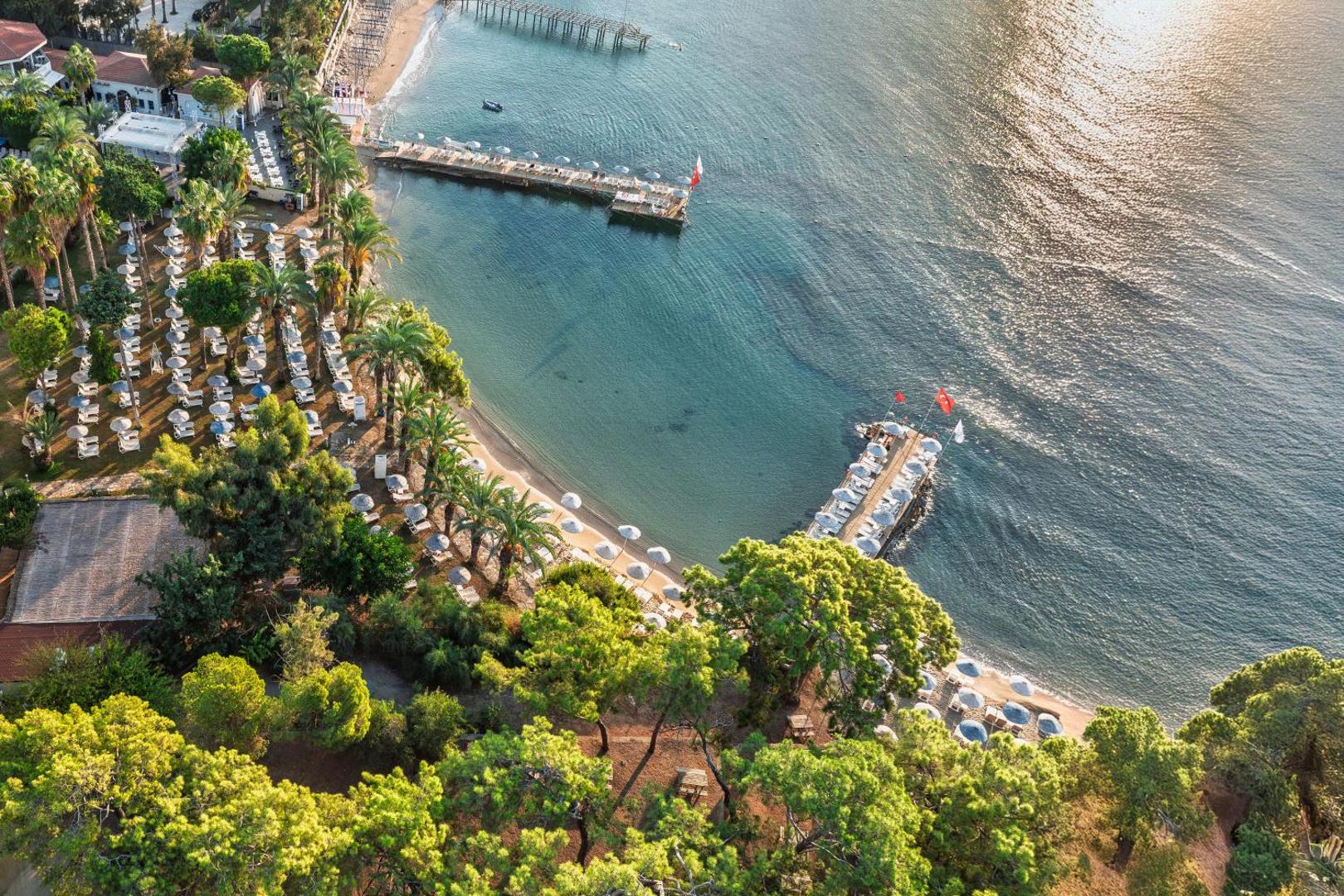 Utopia Resort & Residence pludmales zona no augšas — koka piestātnes, saulessargi un dzidrs ūdens Alānijas reģionā