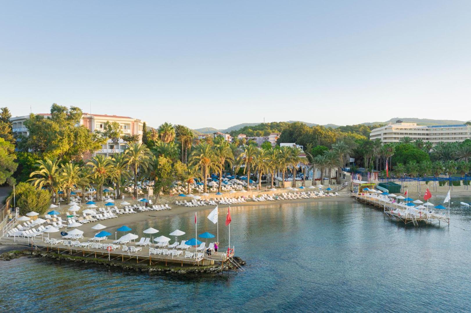 Utopia Resort & Residence viesnīcas ēkas un pludmale ar sauļošanās krēsliem — skats no jūras puses uz kūrorta teritoriju