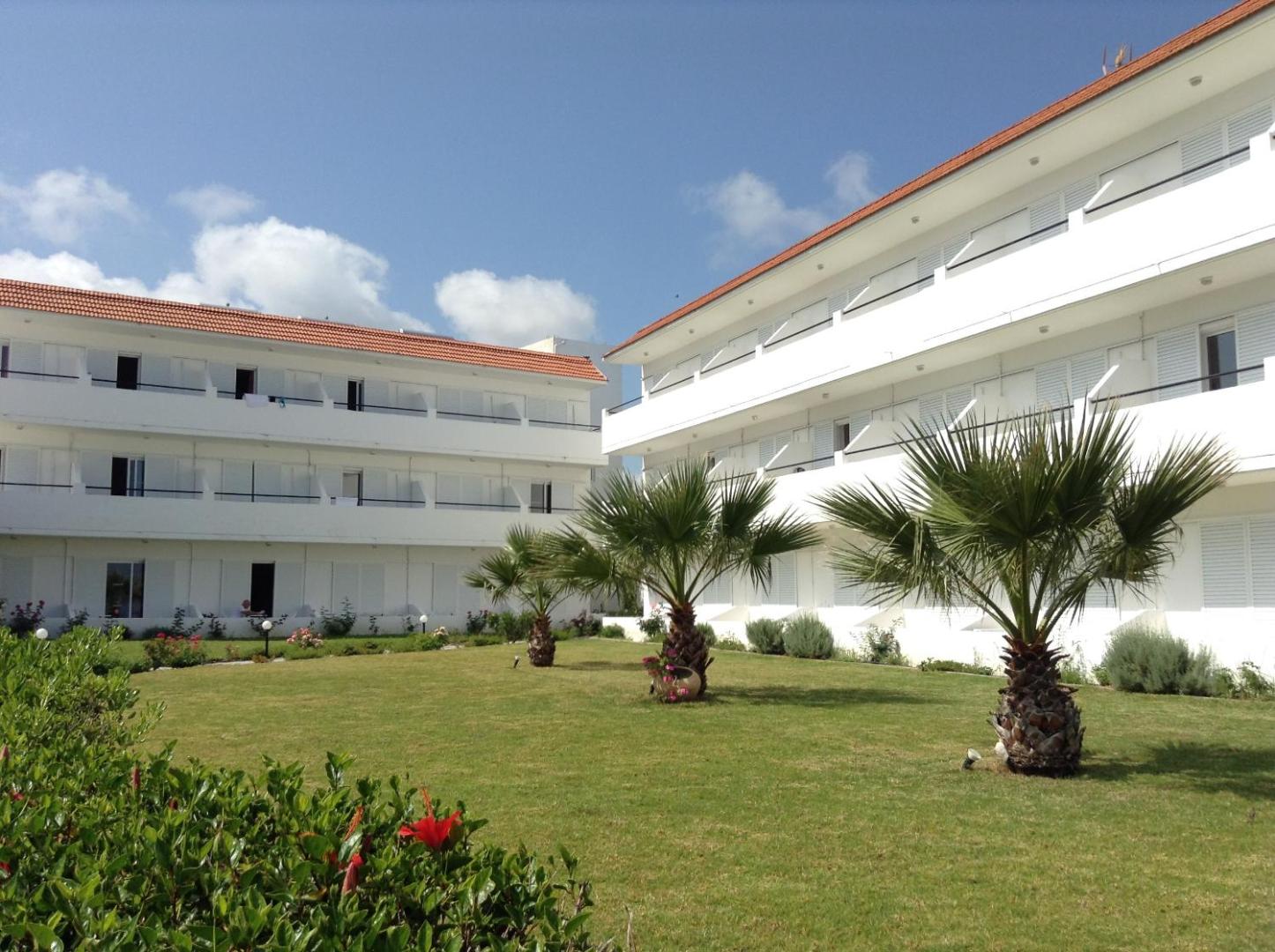 Pylea Beach Hotel numuru korpusi ar balkoniem, kopts zāliens un dekoratīvas palmas saulainā dienā Rodas salā