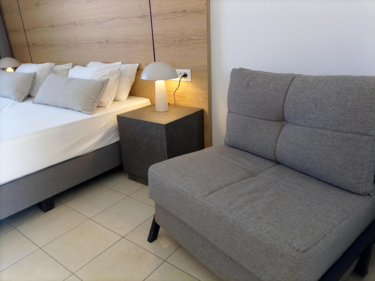 Pylea Beach Hotel numura interjers ar divguļamo gultu, koka galvgali un pelēku atpūtas krēslu Rodas viesnīcā