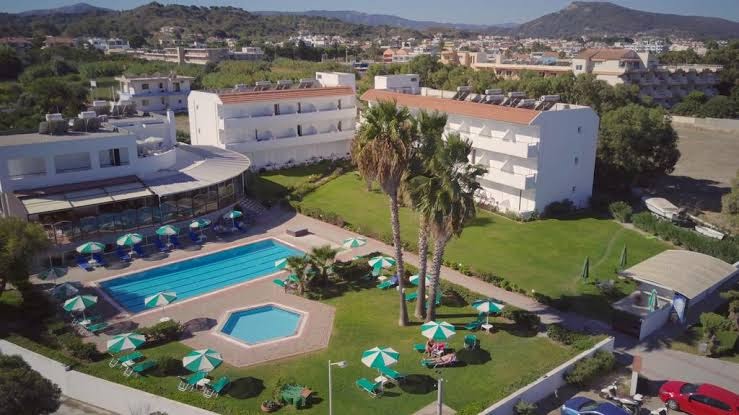 Pylea Beach Hotel teritorija no augšas — galvenais baseins, bērnu baseins, sauļošanās krēsli ar saulessargiem un palmas zaļā zālienā