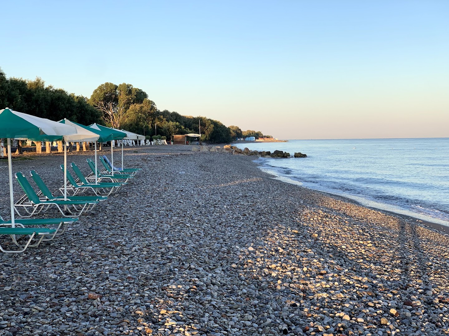 Pylea Beach Hotel pludmales zona ar zaļiem saulessargiem un sauļošanās krēsliem rīta gaismā