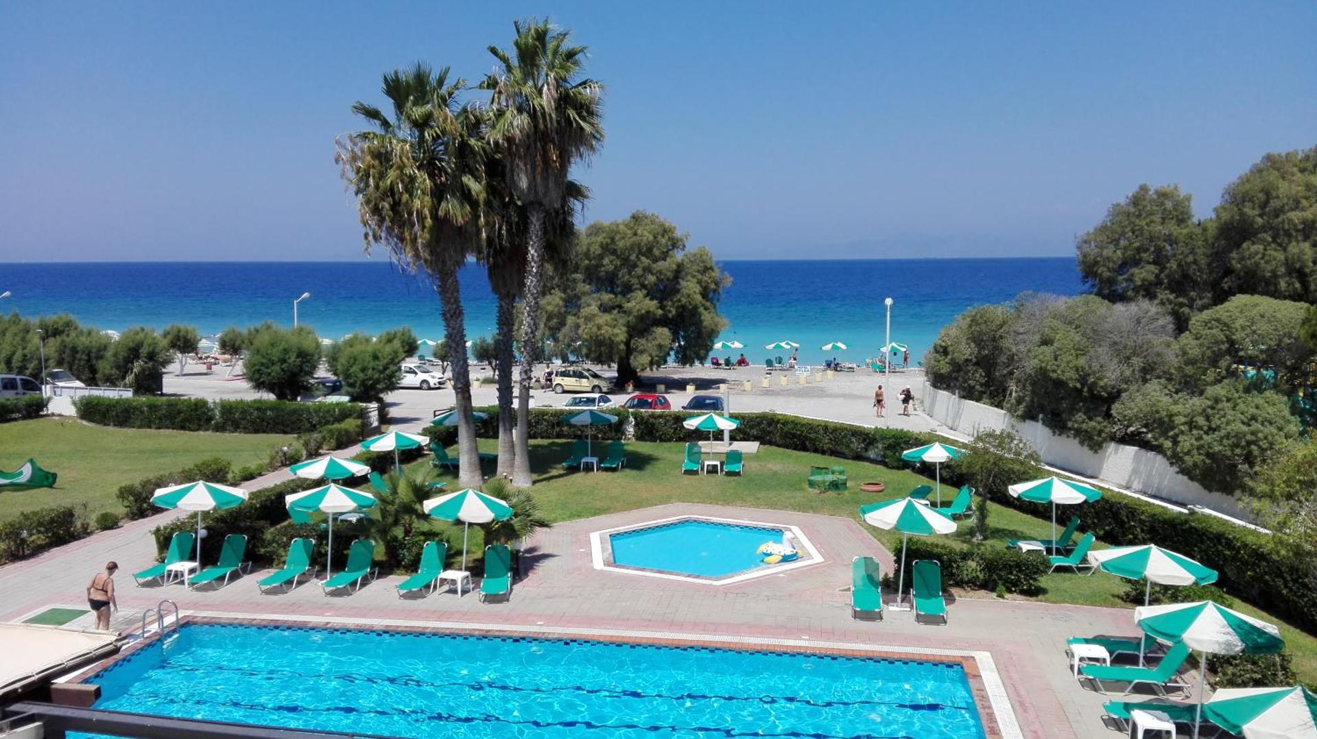 Pylea Beach Hotel skats no augšas uz āra baseinu, atpūtas zonu ar saulessargiem un Egejas jūras piekrasti Rodas salā.