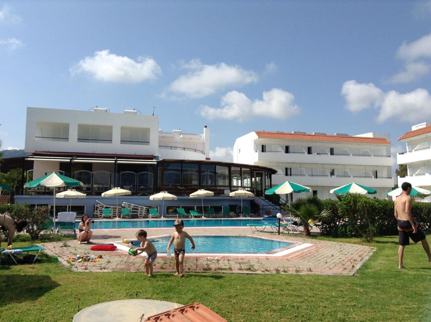 Pylea Beach Hotel viesnīcas ēkas fasāde un bērnu baseins zaļā zālienā, kur rotaļājas bērni saulainā dienā Rodā.