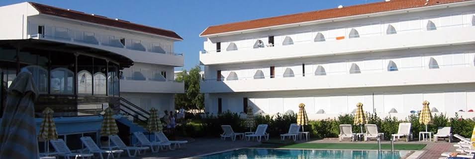 Pylea Beach Hotel āra baseins ar sauļošanās krēsliem un saulessargiem, fonā viesnīcas baltās ēkas un restorāns
