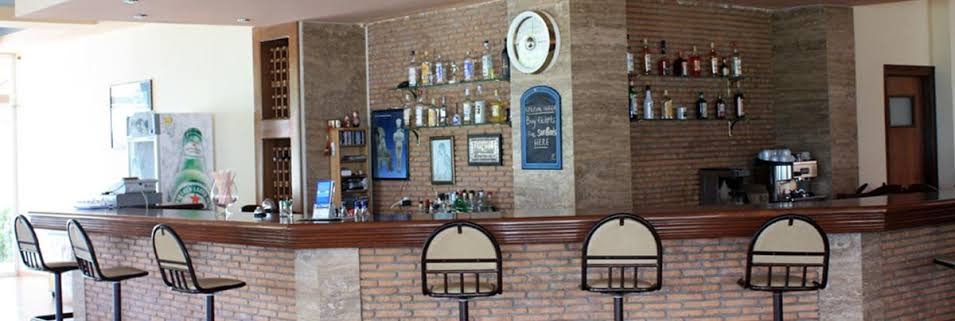 Pylea Beach Hotel bārs Rodas salā ar ķieģeļu apdari, augstiem krēsliem un plašu dzērienu izvēli mājīgā atmosfērā