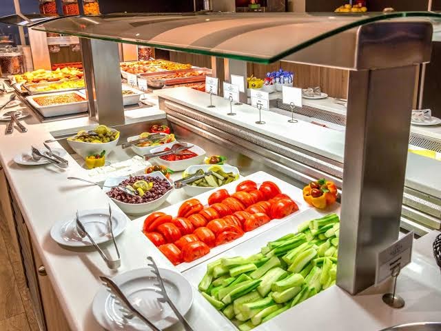 Mercure Rhodes Alexia Hotel & Spa brokastu bufete ar svaigiem dārzeņiem, olīvām, tomātiem un siltajiem ēdieniem restorāna zonā.