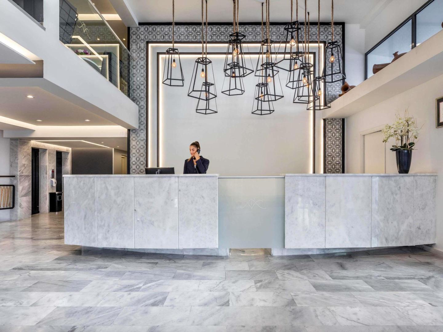 Mercure Rhodes Alexia Hotel & Spa modernā recepcija Rodas pilsētā ar marmora apdari un stilīgiem, industriāla dizaina piekaramajiem gaismekļiem