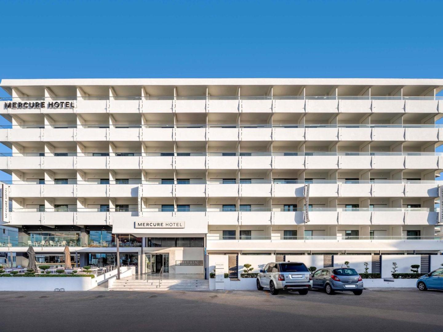 Mercure Rhodes Alexia Hotel & Spa fasāde Rodas pilsētā dienas laikā — moderna daudzstāvu ēka ar balkoniem un ieeju pie pilsētas ielas