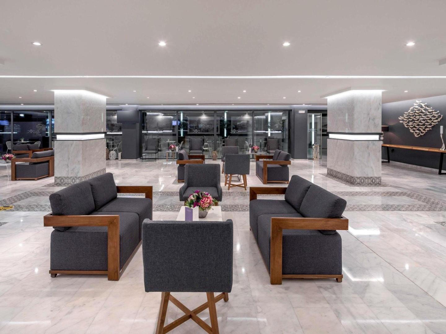 Plašā Mercure Rhodes Alexia Hotel & Spa koptelpa ar tumši pelēkiem dīvāniem, koka akcentiem un spīdīgu marmora grīdu