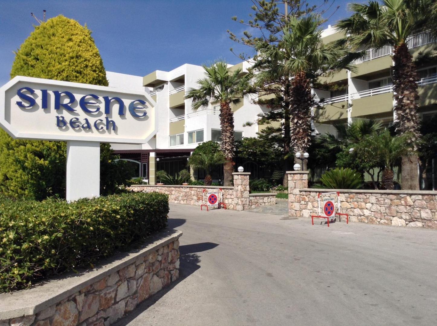 Sirene Beach Hotel galvenā ieeja ar viesnīcas nosaukuma zīmi, palmām un gaišu ēkas fasādi Rodas salā