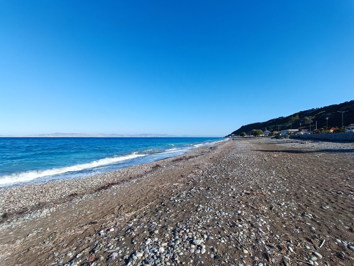 Sirene Beach Hotel oļu pludmale un dzidri zilais jūras ūdens Rodas salā — skats uz piekrasti un kalniem tālumā