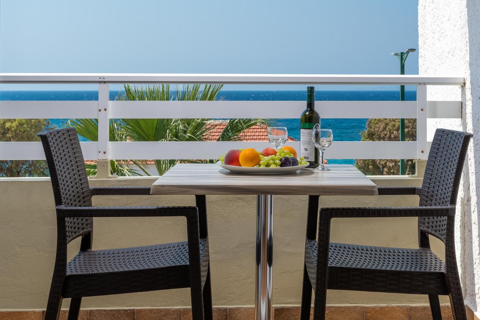 Sirene Beach Hotel balkons ar galdiņu, augļiem un vīnu, no kura paveras tiešs skats uz zilo jūru Rodā
