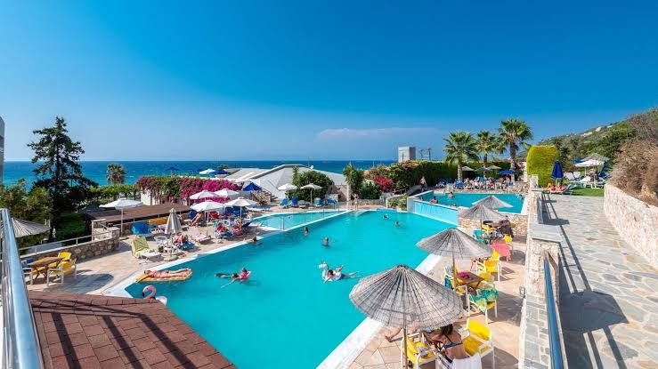 Sirene Beach Hotel galvenais baseins Rodas salā ar skatu uz Egejas jūru, saulessargiem un atpūtas zonu piekrastē