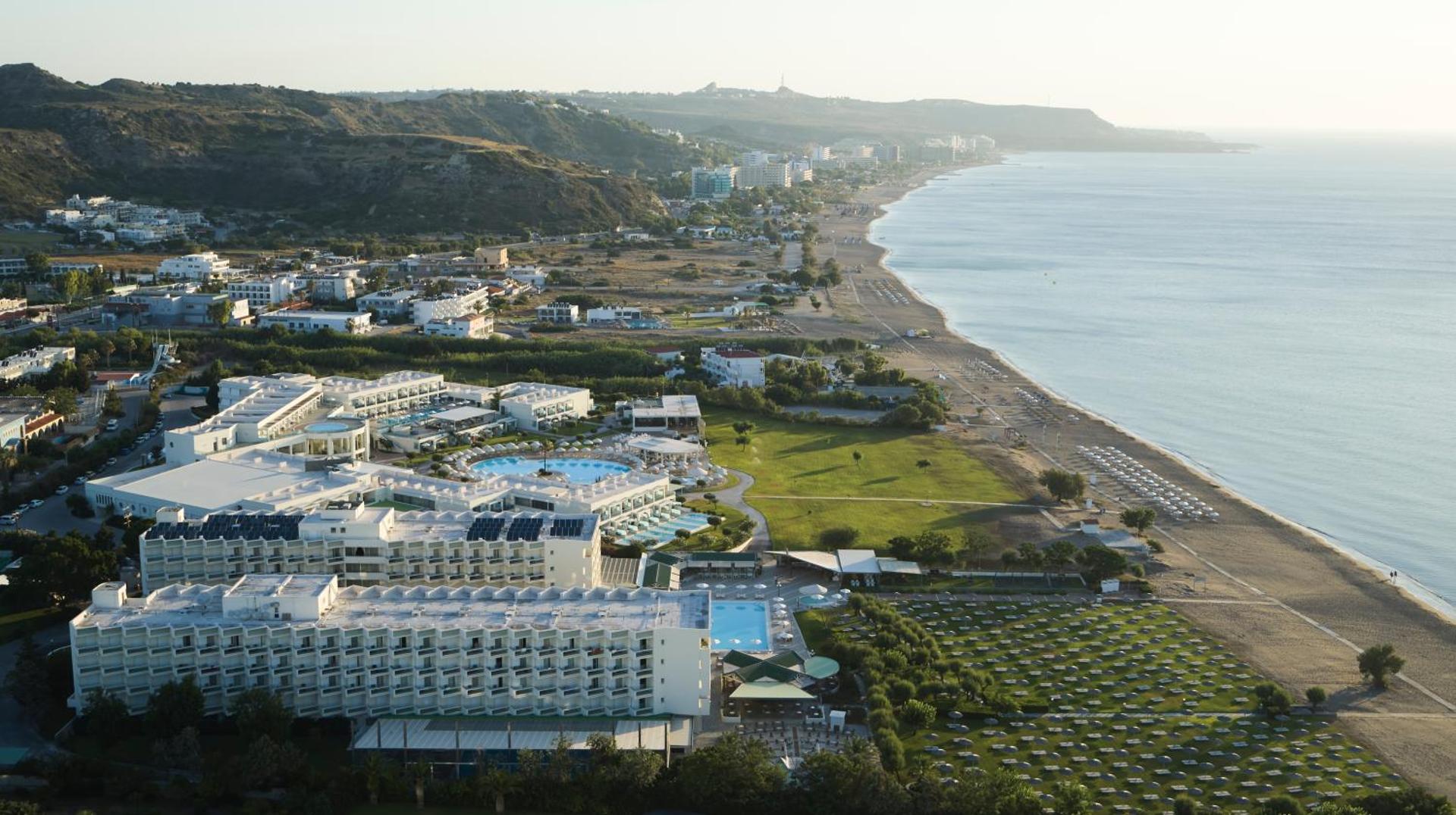 Apollo Beach viesnīcas panorāmas skats Faliraki piekrastē Rodas salā — plaša teritorija ar baseiniem, zaļo zonu un tiešu piekļuvi smilšu pludmalei.