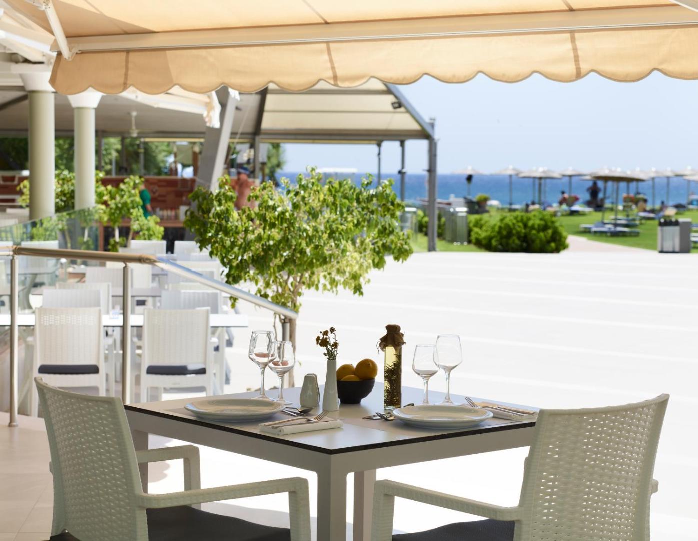 Apollo Beach restorāna āra terase ar klātiem galdiem un skatu uz dārzu un jūru Faliraki