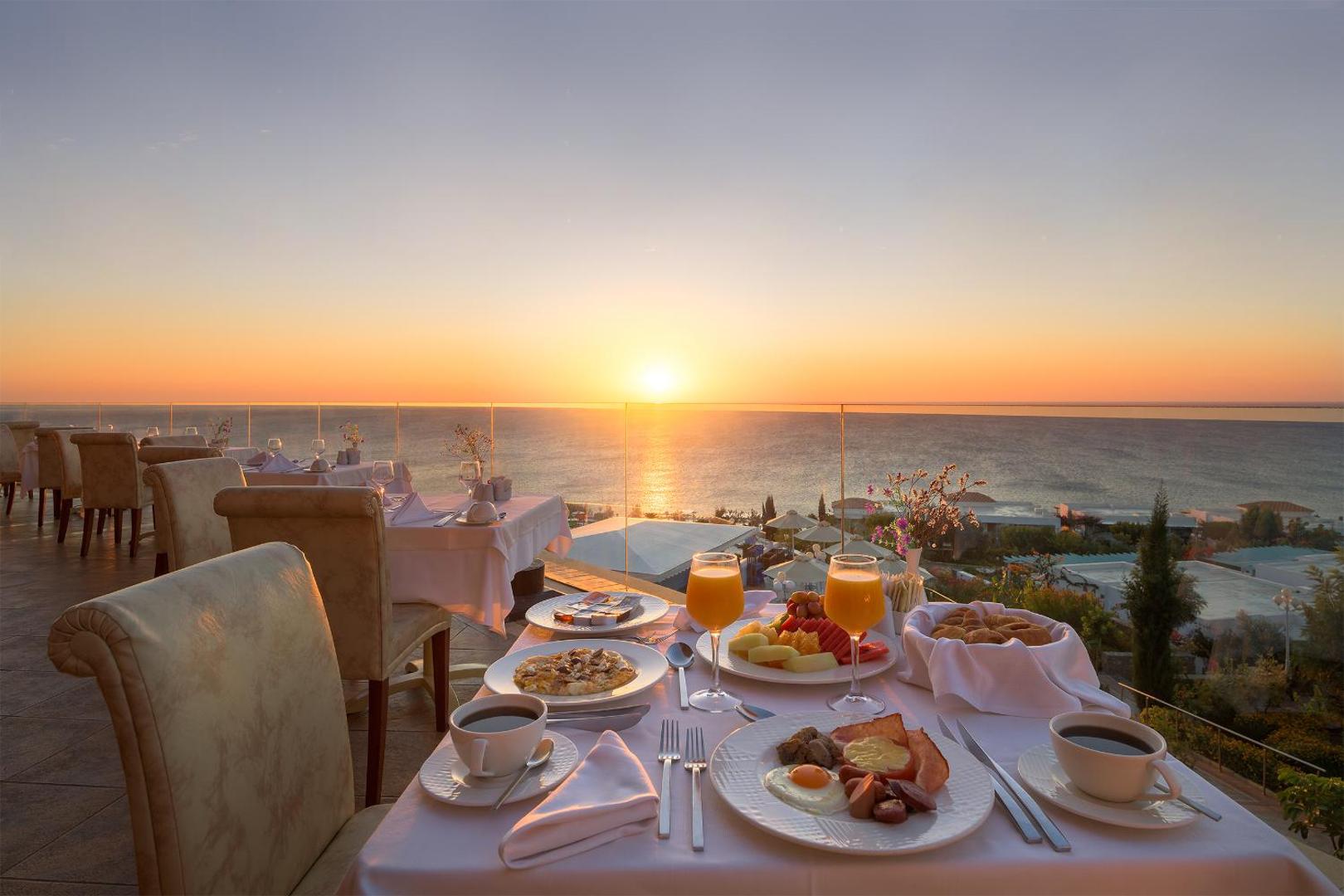 Atrium Prestige Thalasso Spa Resort & Villas restorāna terase saulrieta laikā Rodas salā — klāts galds ar brokastīm un skatu uz jūru