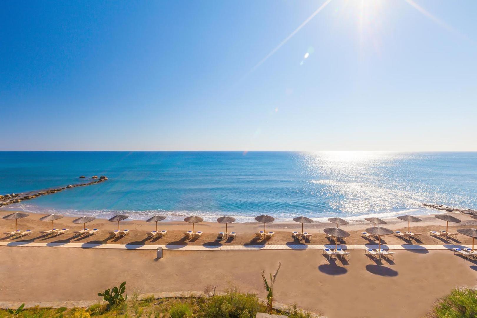Atrium Prestige Thalasso Spa Resort & Villas privātā smilšu pludmale Rodas salā ar saulessargiem un gultām saulrietā