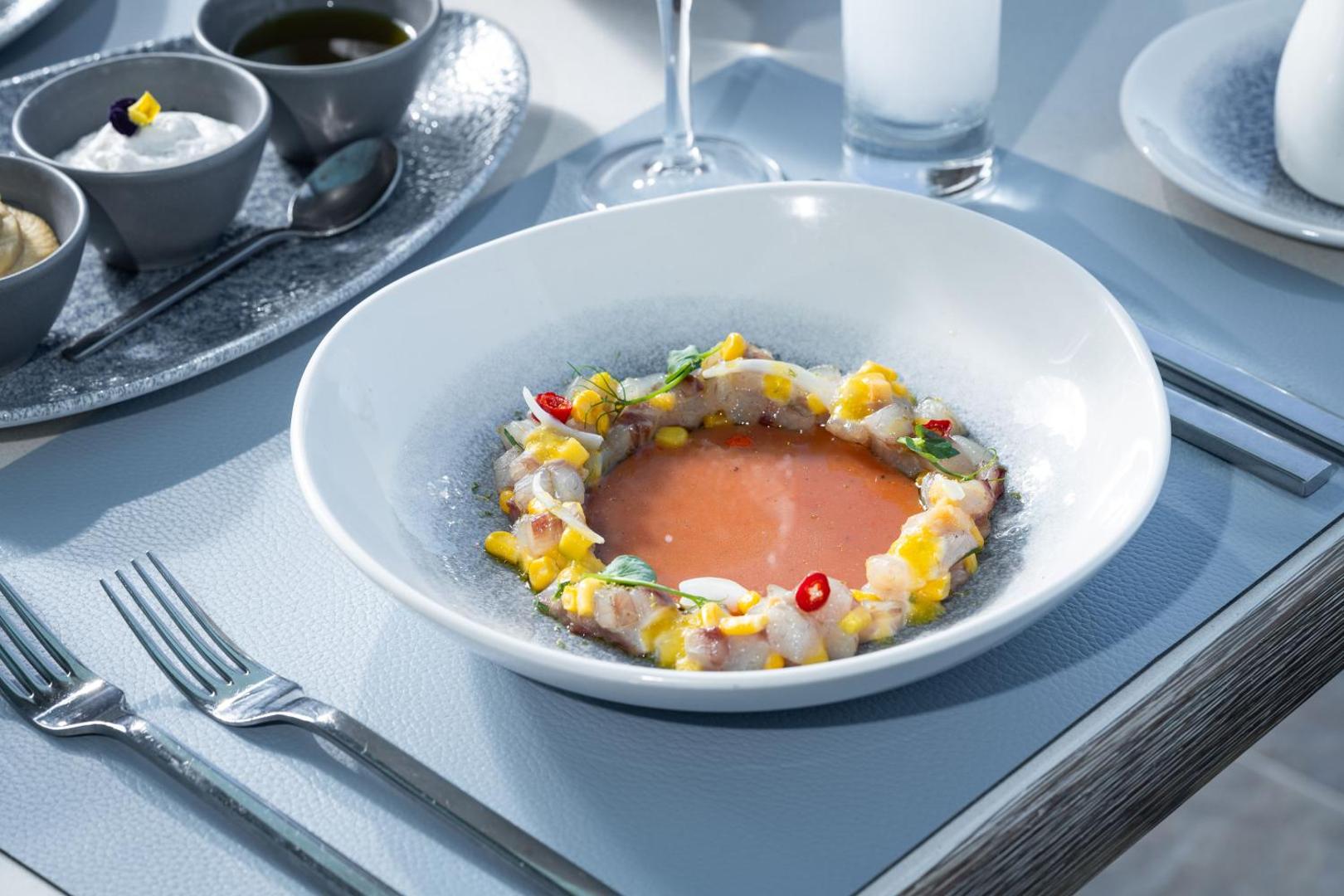 Atrium Prestige Thalasso Spa Resort & Villas restorāna izsmalcināts jūras velšu ēdiens ar kukurūzu un čili, pasniegts uz gaiši zila galda klājuma.