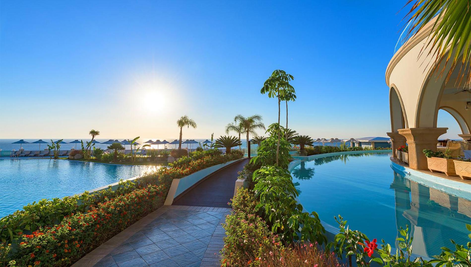 Atrium Prestige Thalasso Spa Resort & Villas dārza taka gar baseinu ar skatu uz jūru un palmām Rodas piekrastē