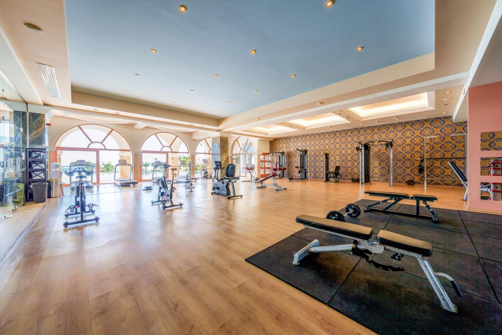 Atrium Prestige Thalasso Spa Resort plaša fitnesa zāle ar moderniem trenažieriem un lieliem logiem Rodā