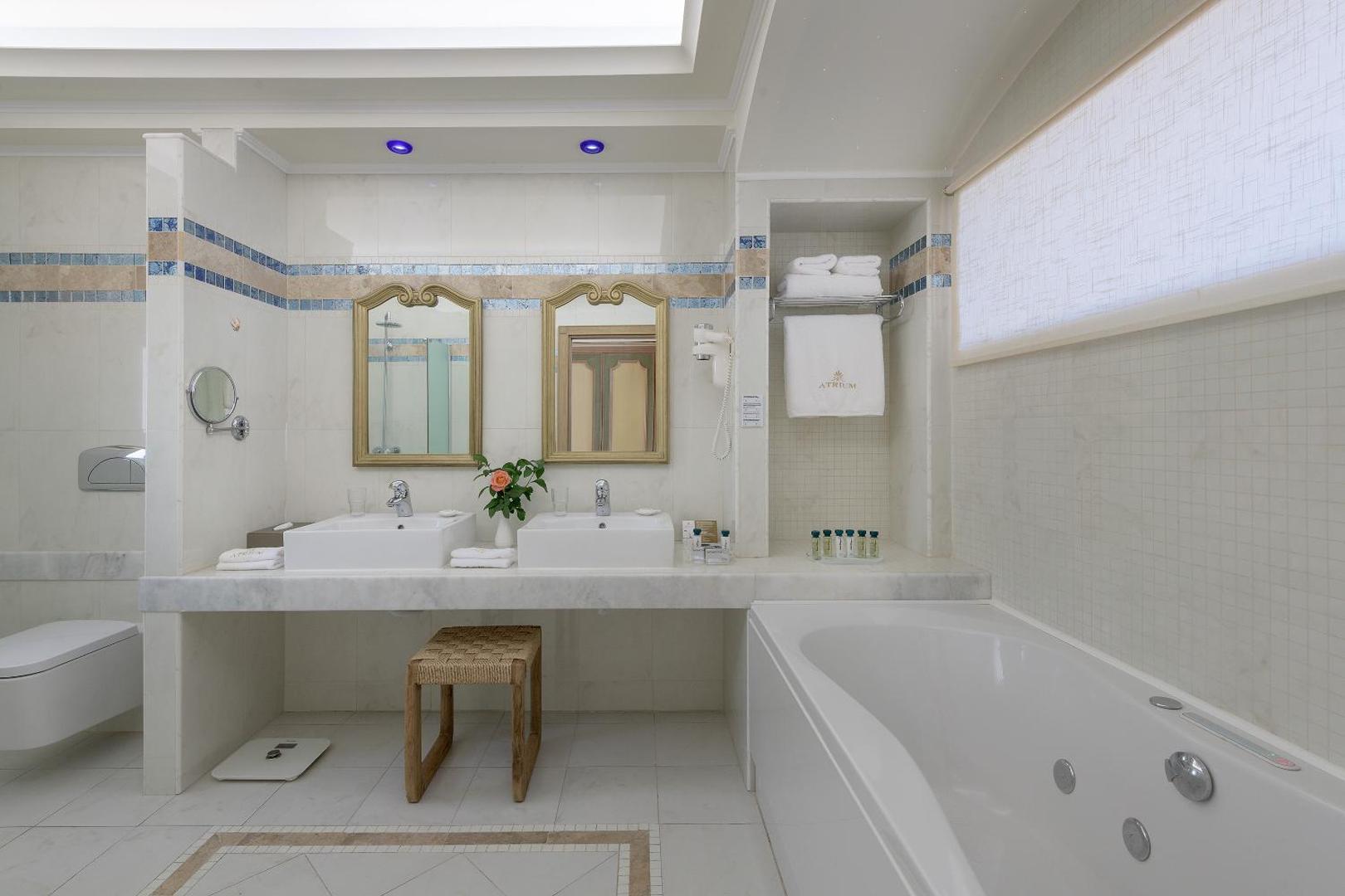 Gaiša un plaša Atrium Prestige Thalasso Spa Resort vannasistaba ar divām izlietnēm, lielu spoguli, vannu un marmora apdares elementiem.