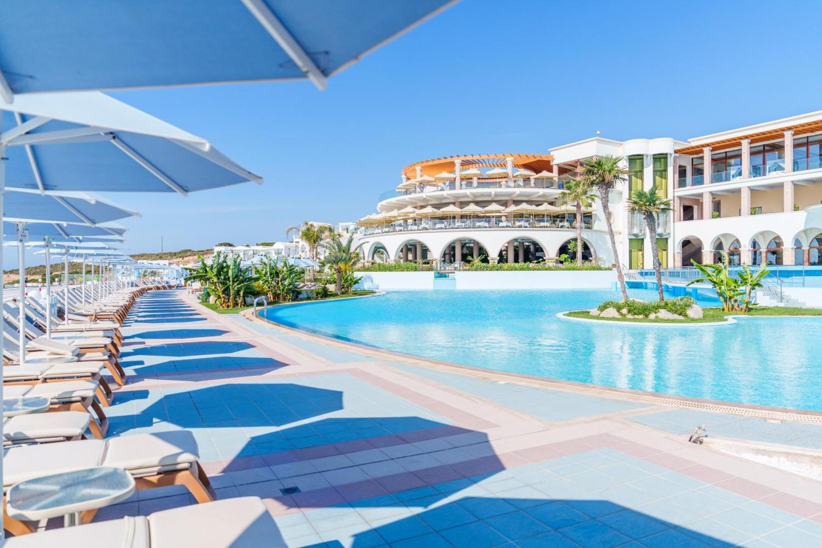 Atrium Prestige Thalasso Spa Resort & Villas galvenais baseins un viesnīcas arhitektūra Rodā — sauļošanās krēsli un saulessargi pie ūdens
