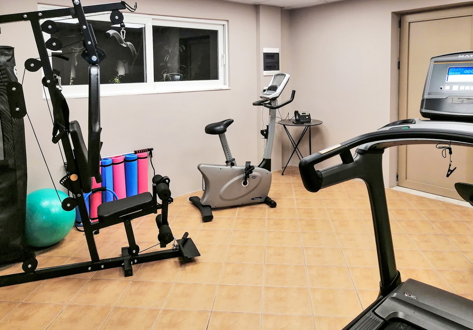 Viesnīcas White Olive Premium Lindos sporta zāle ar velotrenažieri, jogas paklājiņiem un skatu pa logu uz Rodas piekrastes apkārtni