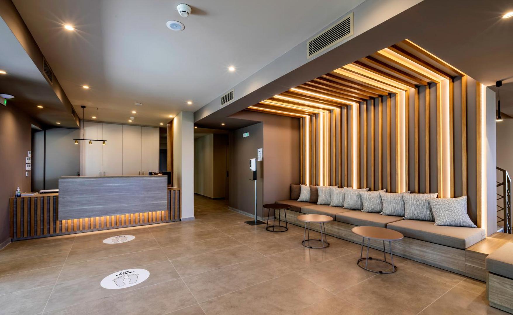 White Olive Premium Lindos viesnīcas lobby un recepcijas zona ar modernu koka apdari, apgaismojumu un atpūtas dīvānu
