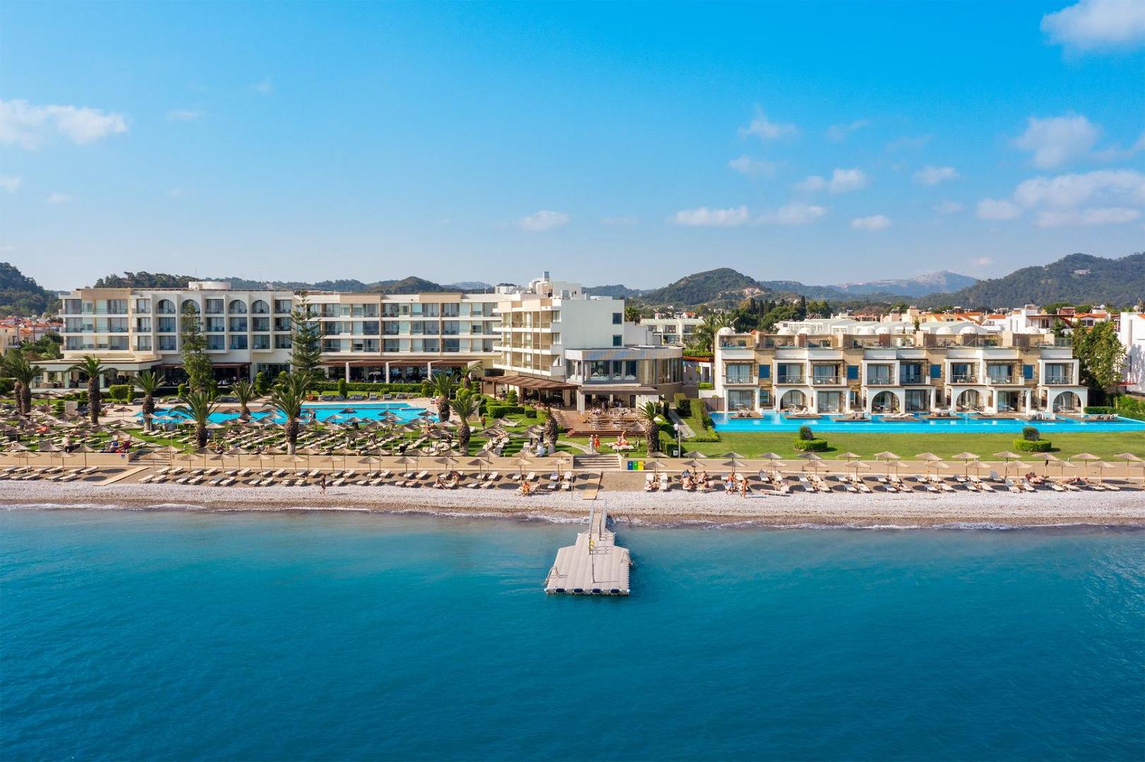 The Ixian Grand & All Suites skats no jūras puses uz galveno ēku, peldošo piestātni un saulaino pludmales zonu Rodā.