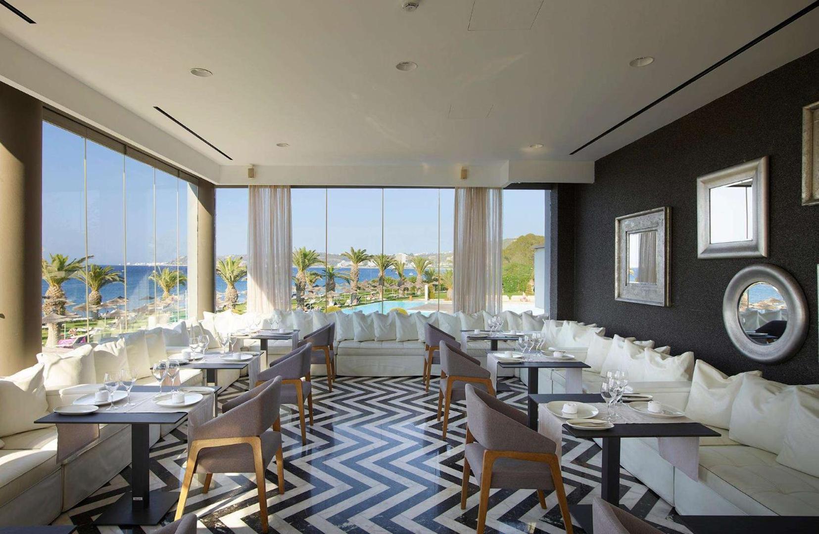 The Ixian Grand & All Suites dizaina restorāns ar panorāmas logiem un skatu uz dārzu un baseinu Rodas salā