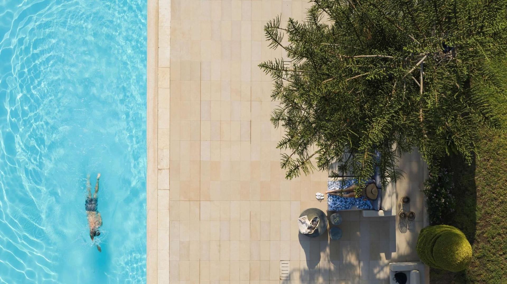 The Ixian Grand & All Suites baseina mala un atpūtas zona zem kokiem Rodas piekrastē — skats no putna lidojuma