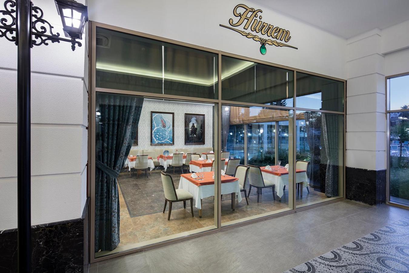 Dosinia Luxury Resort a la carte restorāns Hürrem ar eleganti klātiem galdiem un mākslas darbiem pie sienām Kemeras reģionā