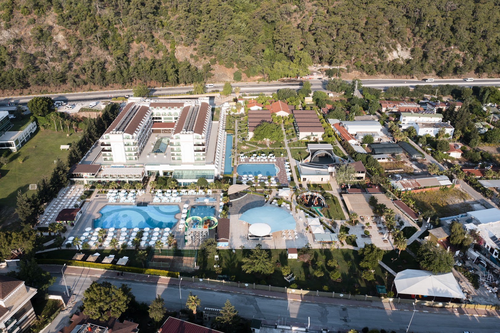 Dosinia Luxury Resort teritorijas plāns no augšas, parādot baseinus, bērnu laukumus un dārzu starp kalniem un jūru