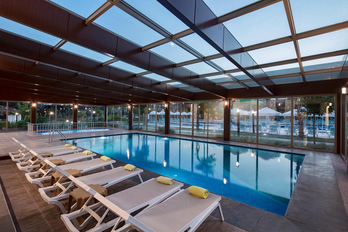Dosinia Luxury Resort iekštelpu baseins ar stikla jumtu un sienām, gaiši sauļošanās krēsli ar dzelteniem dvieļiem