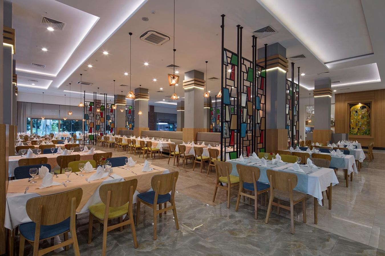 Dosinia Luxury Resort galvenais restorāns ar modernu interjeru, krāsainām stikla starpsienām un eleganti klātiem galdiem vakariņām