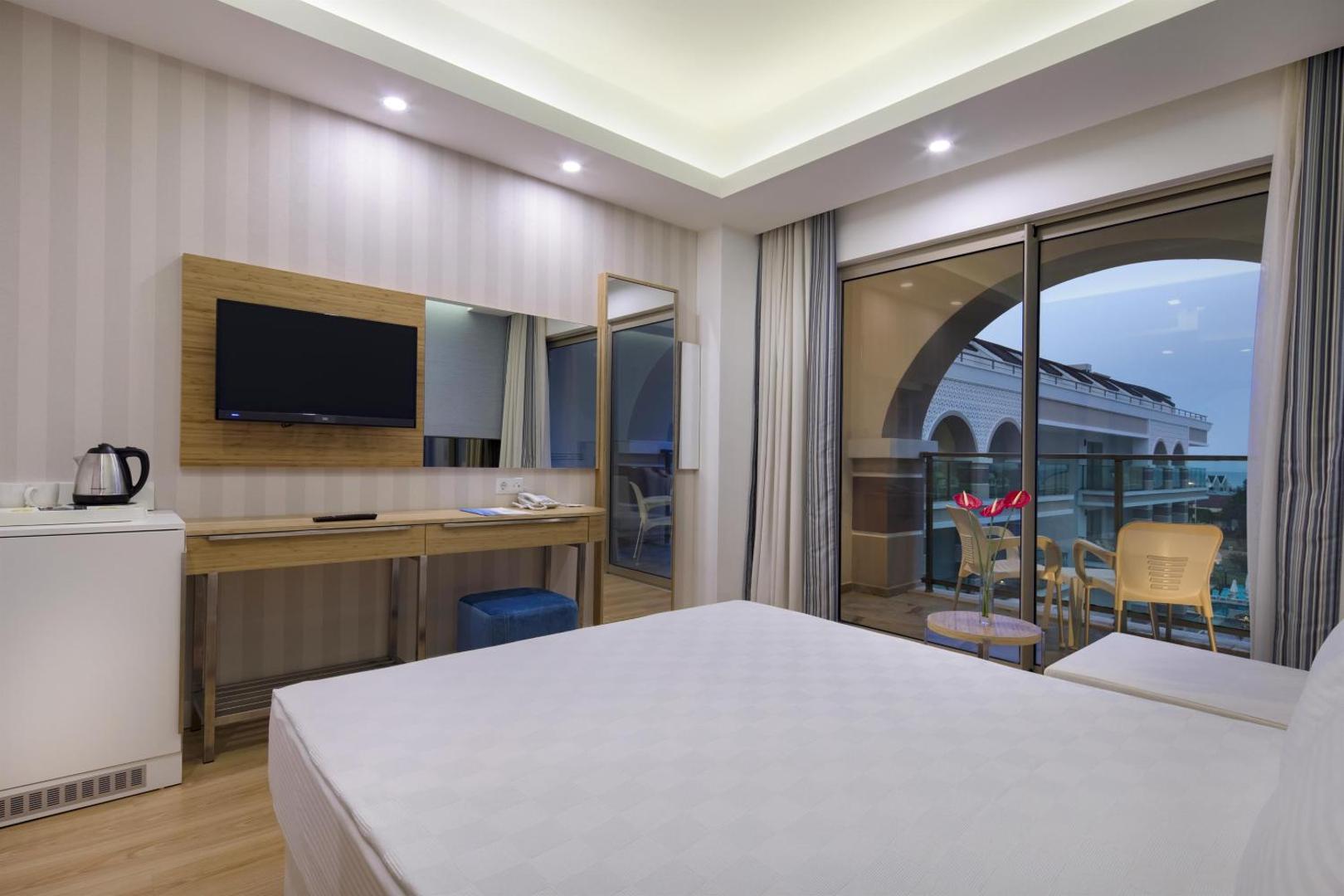 Dosinia Luxury Resort viesnīcas numura skats vakarā uz balkonu un kaimiņu ēku arhitektūru Kemeras piekrastē — mājīgs apgaismojums un elegants dizains