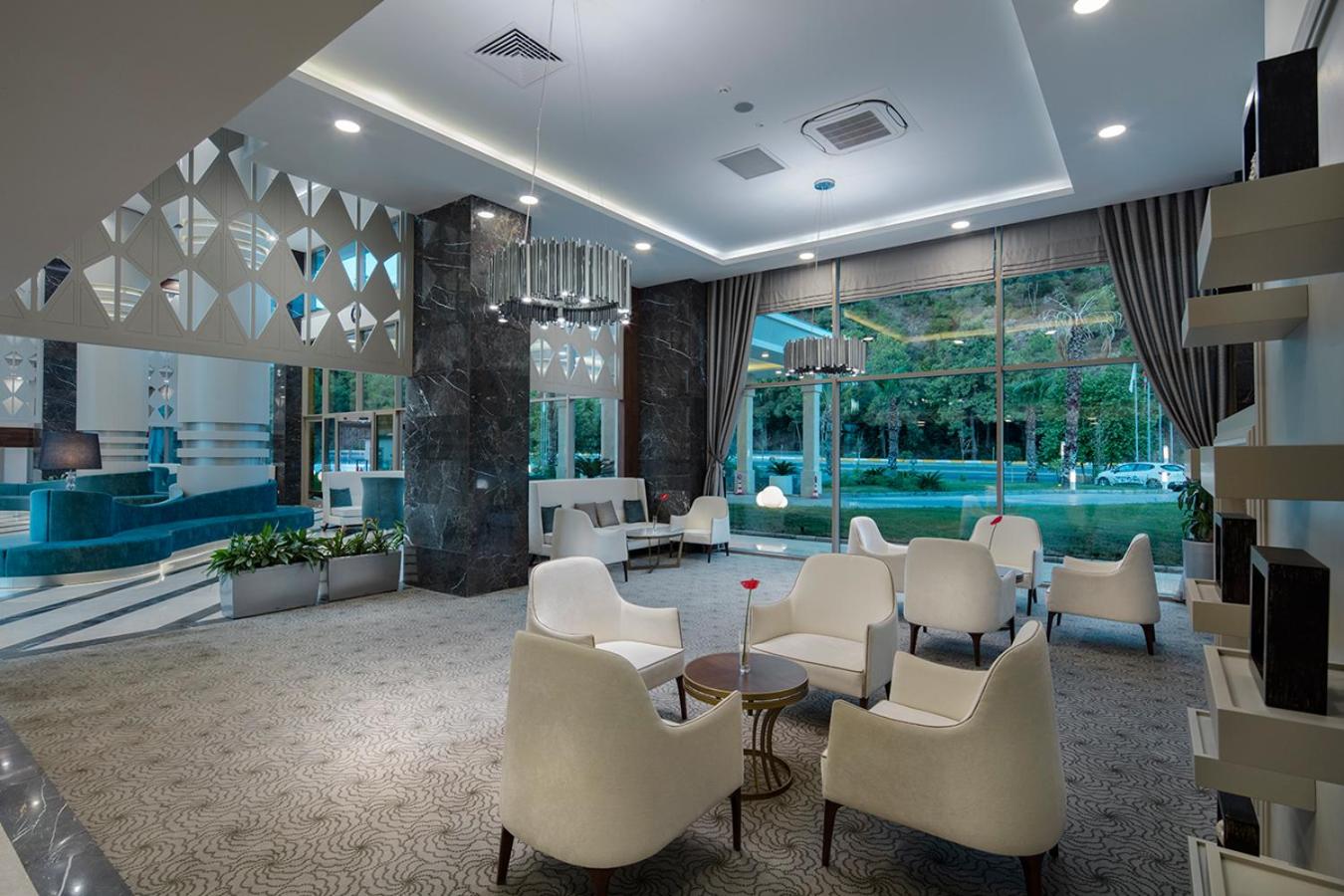 Dosinia Luxury Resort viesnīcas vestibils ar elegantiem krēsliem, marmora kolonnām un lieliem logiem uz dārzu Kemeras reģionā, Turcijā