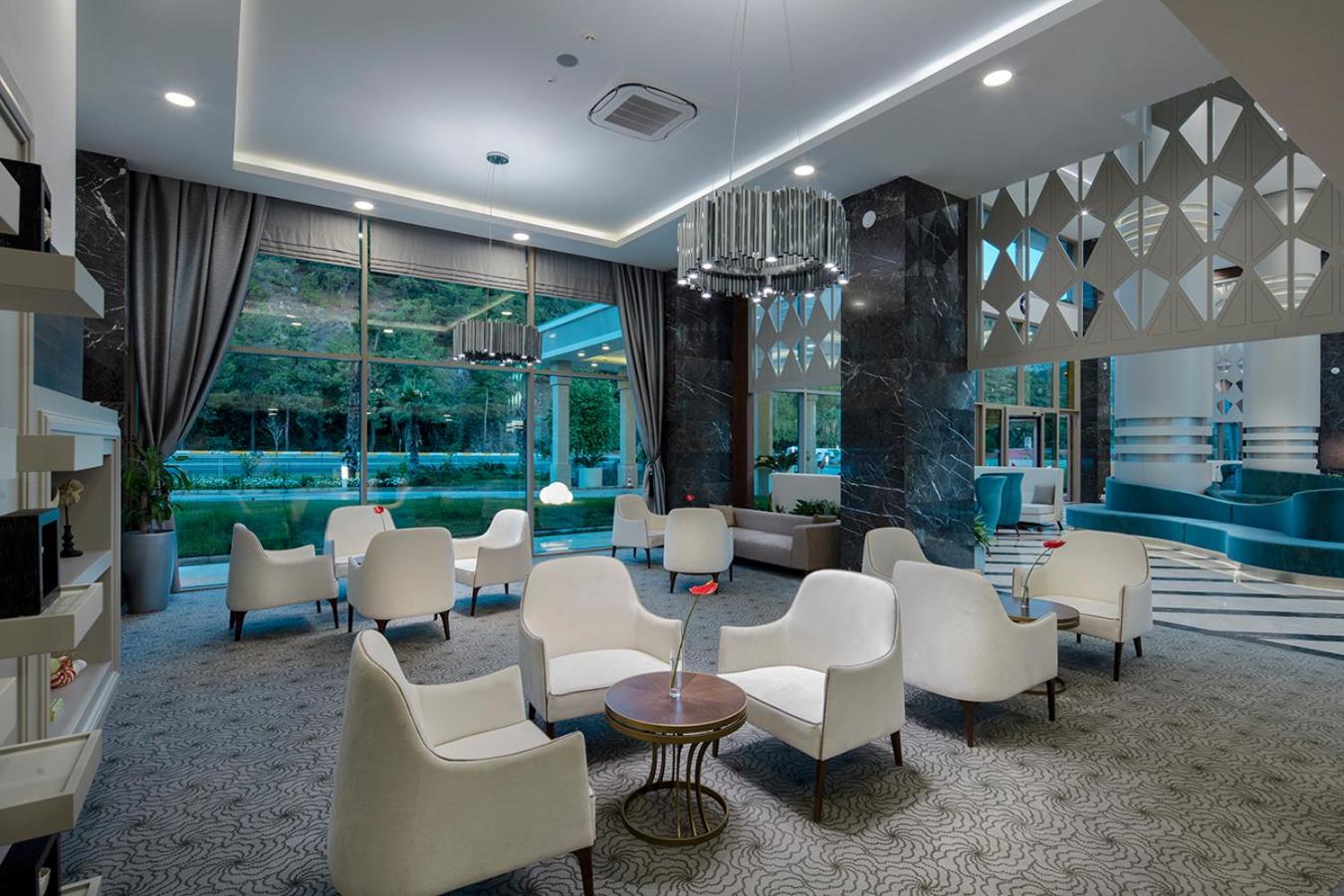 Dosinia Luxury Resort plašā lobby zona ar modernām mēbelēm, dizaina lustrām un skatu uz viesnīcas apzaļumoto teritoriju