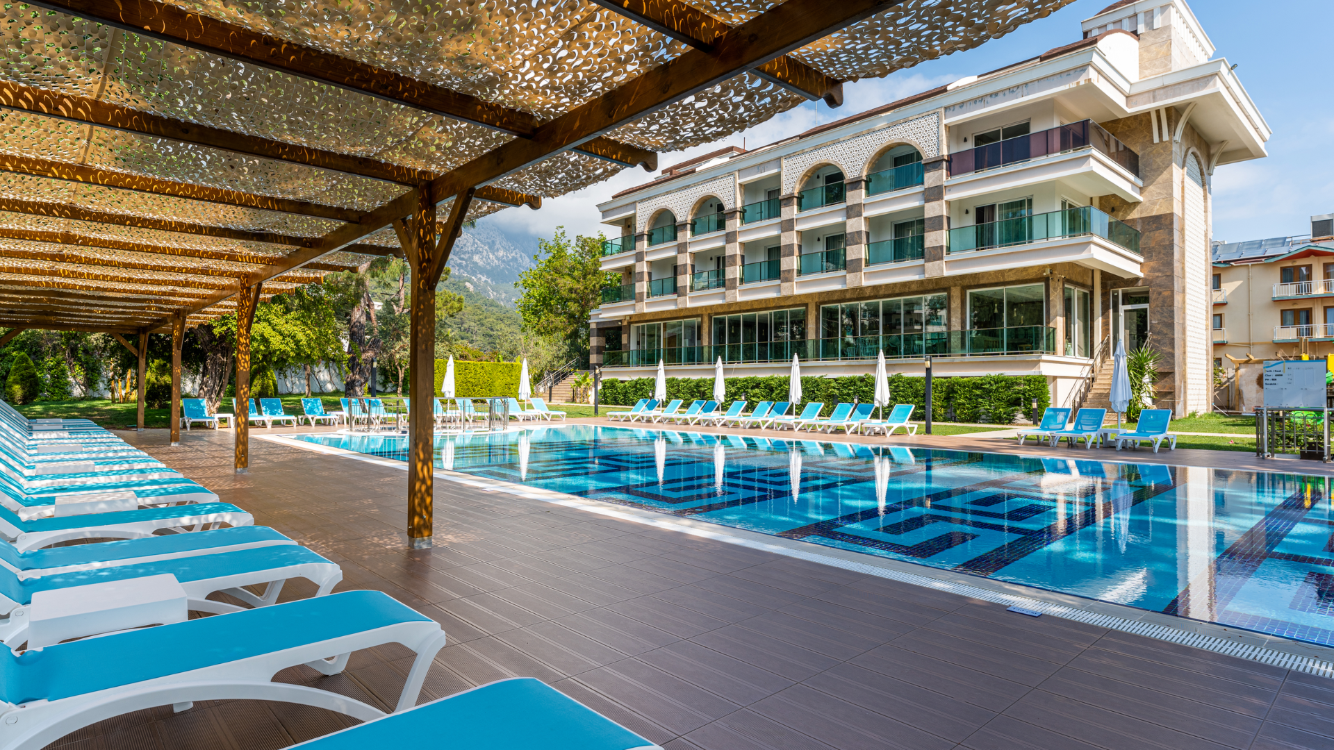 Dosinia Luxury Resort āra baseins ar ziliem sauļošanās krēsliem zem koka nojumes un skatu uz viesnīcas korpusu