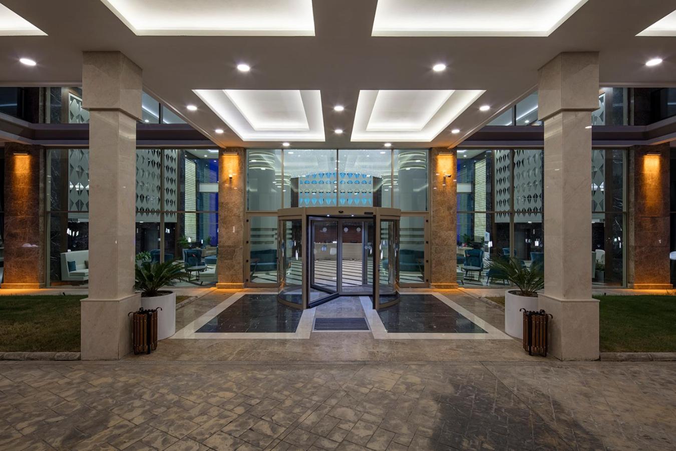Dosinia Luxury Resort modernā ieeja un vestibils vakarā ar stikla rotējošām durvīm un elegantu apgaismojumu