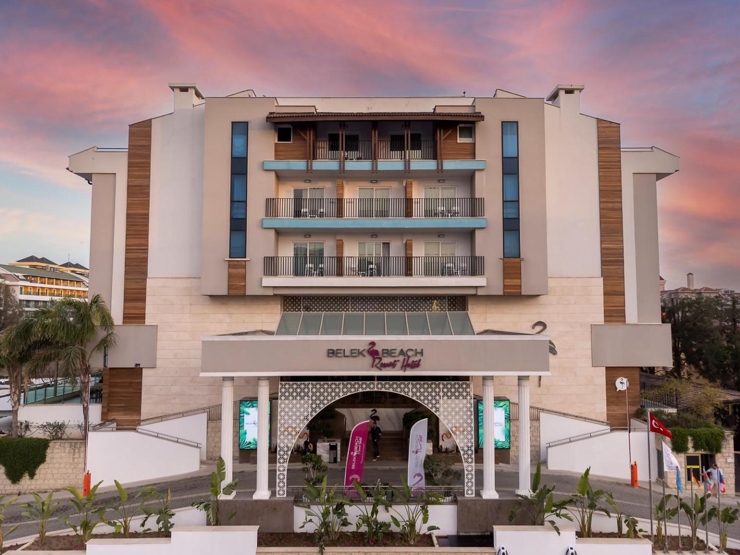 Belek Beach Resort galvenā ieeja un fasāde saulrieta laikā Belekā — moderna arhitektūra ar balkoniem un koka elementiem