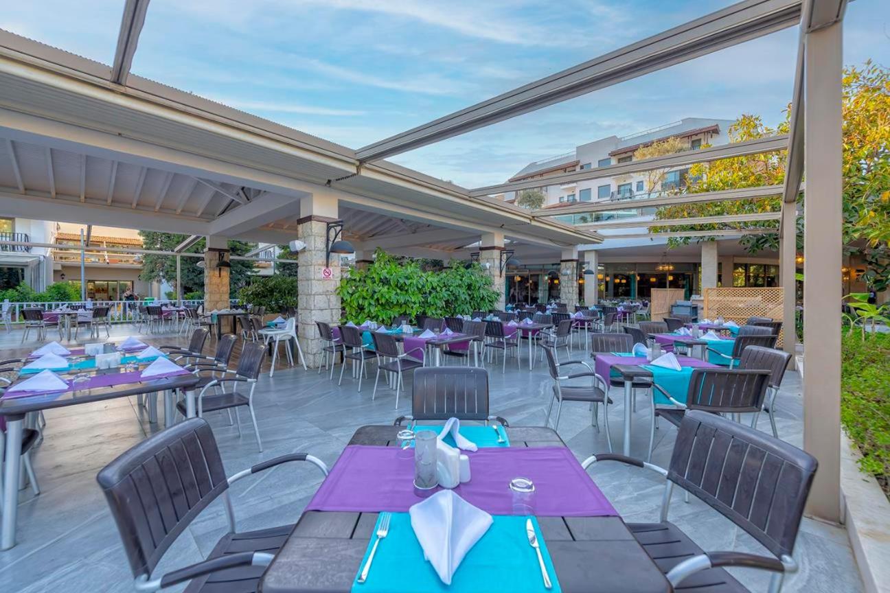 Belek Beach Resort āra restorāna terase ar galdiņiem un krēsliem zem nojumes pie viesnīcas ēkas