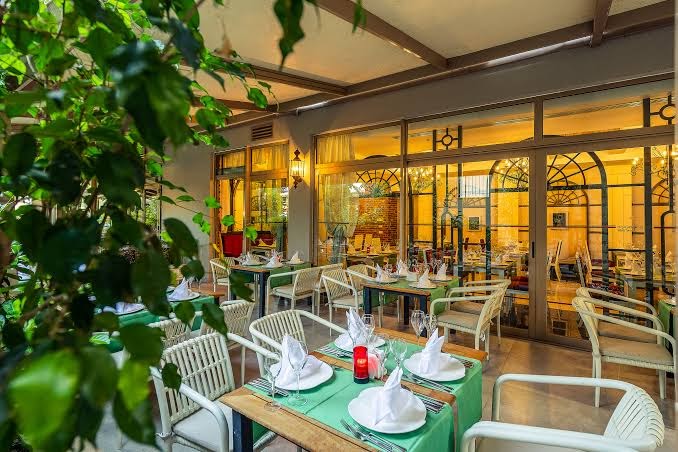 Belek Beach Resort iekštelpu restorāns ar zaļiem galdautiem un dekoratīviem augiem mājīgā apgaismojumā