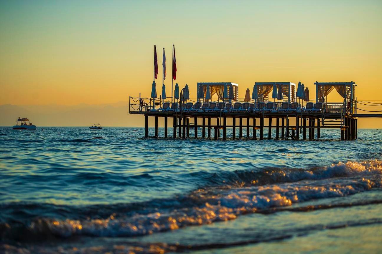 Belek Beach Resort koka mols ar atpūtas nojumēm un sauļošanās krēsliem Vidusjūrā saulrieta laikā