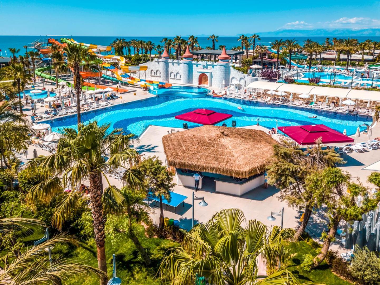 Belek Beach Resort plašā teritorija ar baseiniem, ūdens slidkalniņiem un bāru piekrastē zem zilām debesīm