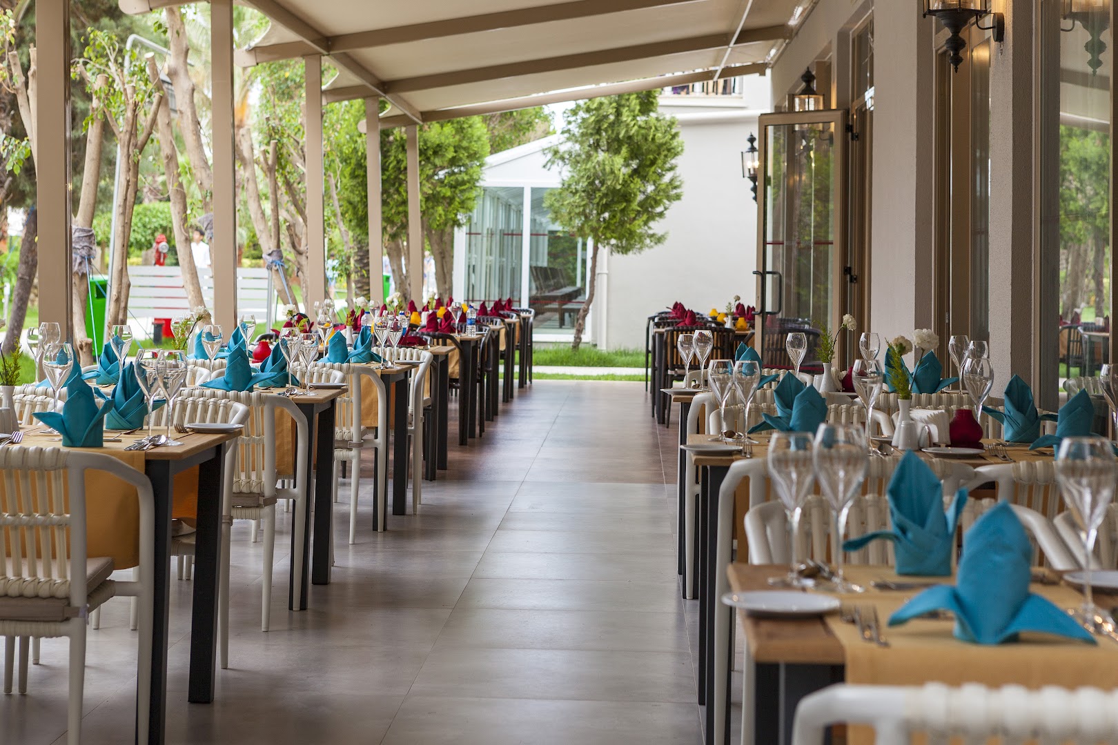 Belek Beach Resort restorāna zona ar eleganti klātiem galdiem un zilām salvetēm gaišā, atvērtā terasē