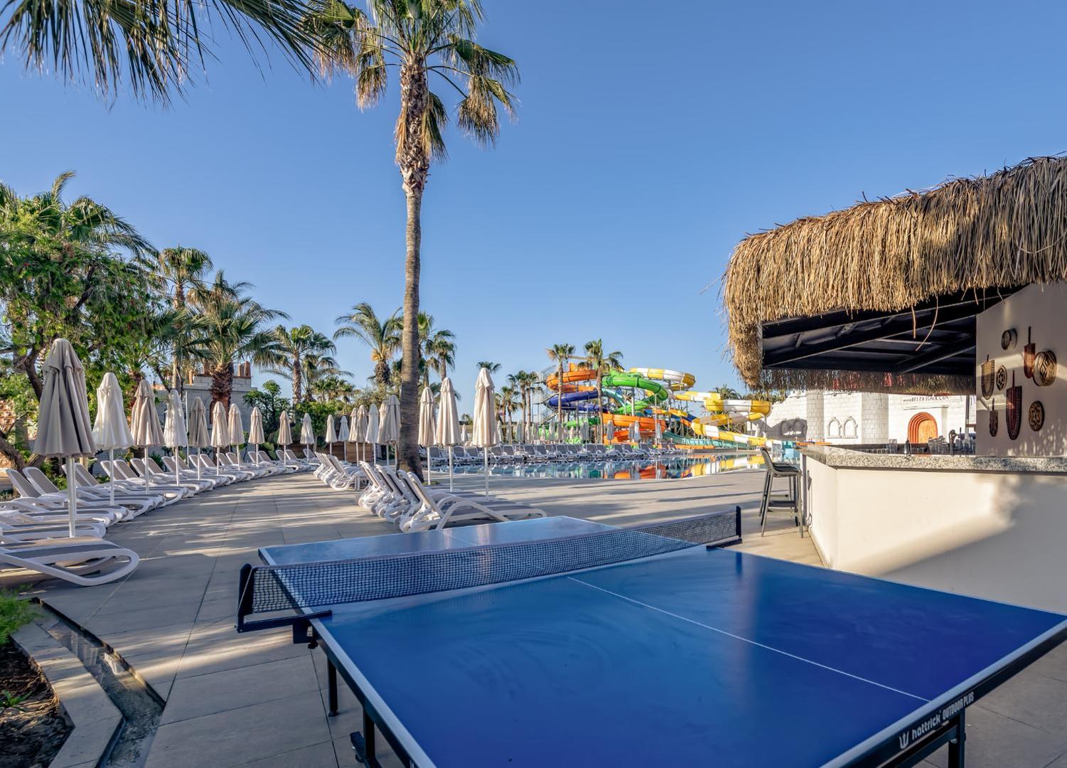 Belek Beach Resort āra atpūtas zona ar galda tenisu, sauļošanās krēsliem un skatu uz akvaparku un palmu dārzu Belekā.