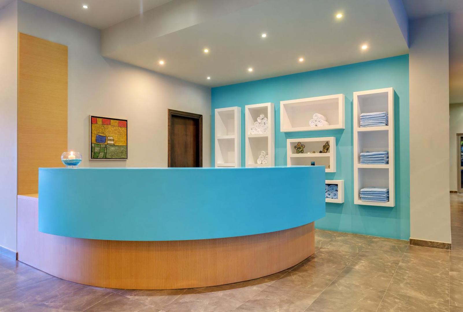 Apollo Blue Hotel spa centra recepcija ar gaiši zilu leti un dvieļu plauktiem — moderna un mājīga sagaidīšanas zona viesiem