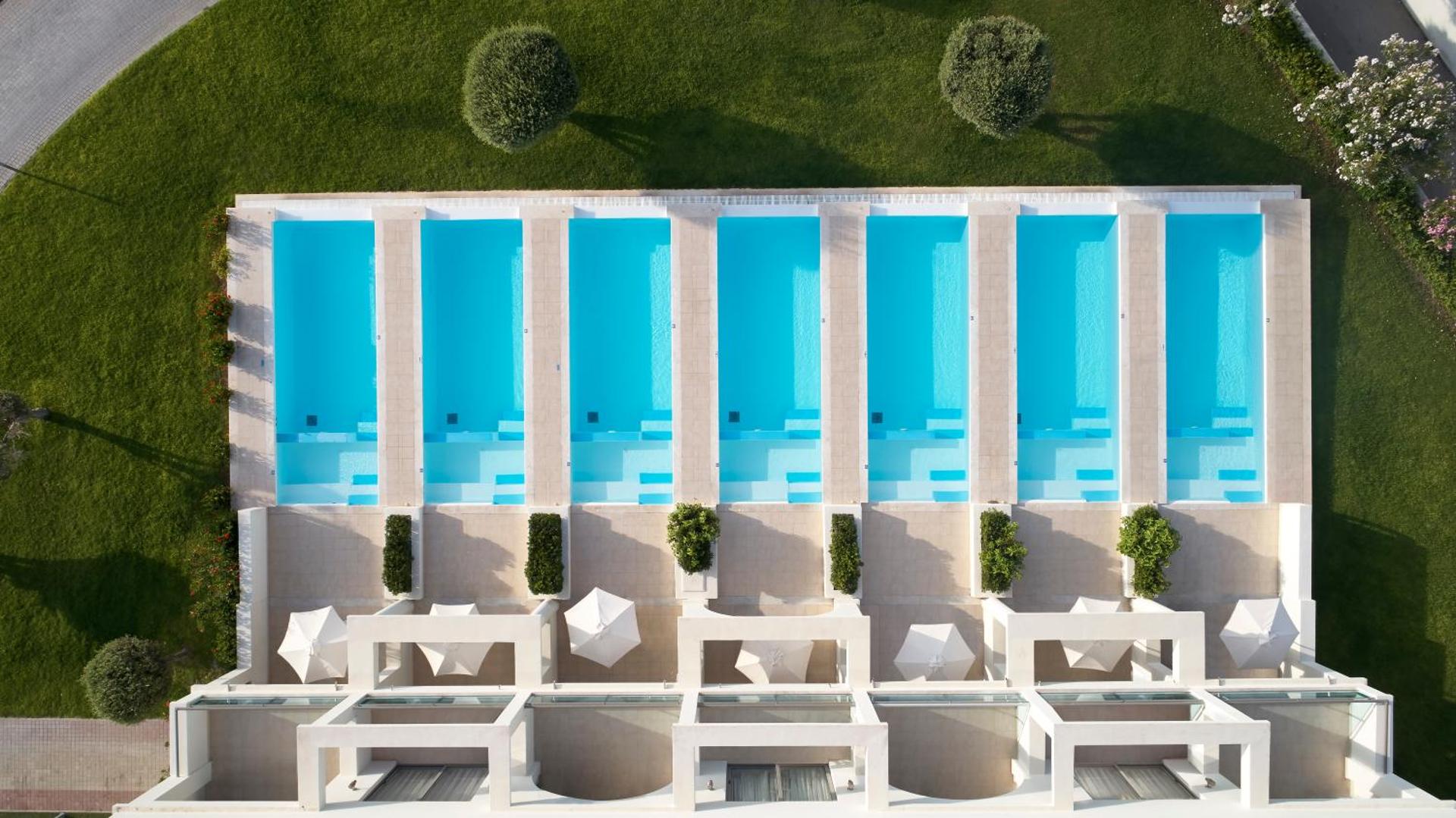 Skats no augšas uz Apollo Blue Hotel numuriem ar tiešu piekļuvi baseinam — privātas terases ar saulessargiem un koptu zālienu